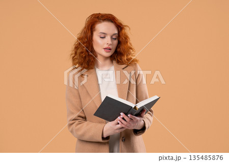 Ginger businesswoman or student reading book with smile on beige. Discovery time 135485876