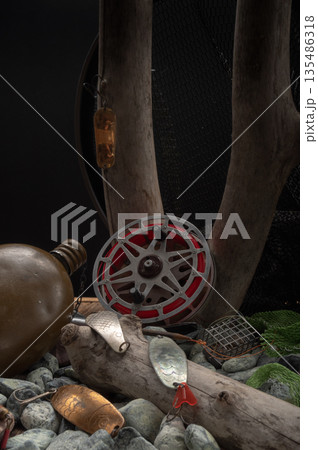 Vintage Soviet fishing gear with an old reel and predator lures placed on stones and wooden branches. 135486318