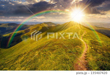path through the grassy mountain ridge at sunset. beautiful summer landscape in fine weather with cloudy sky over green alpine meadow in evening light. leadership corporate wallpaper under the rainbow 135487420