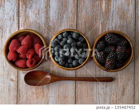Fresh Raspberries, Blueberries, and Blackberries in Wooden Bowls with Spoon 135487452