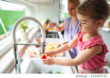 Little chef washing vegetables in a sunny kitchen Little chef washing vegetables in a sunny kitchen 135487535