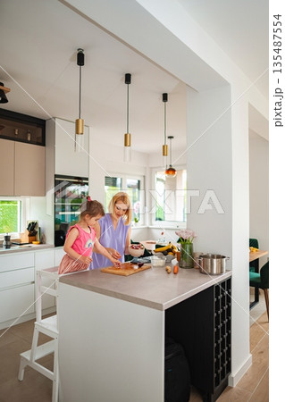 Mother and daughter cooking together in a bright kitchen Mother and daughter cooking together in a bright kitchen 135487554