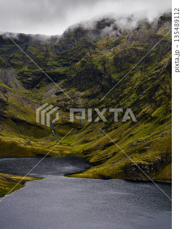 Lake nestled in a lush green valley with a cascade in National Park, on a cloudy day. 135489112