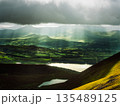 Sunlight streams through dark clouds, illuminating the green hills and fields of Killarney National Park. Lakes reflect the light in the foreground. 135489125