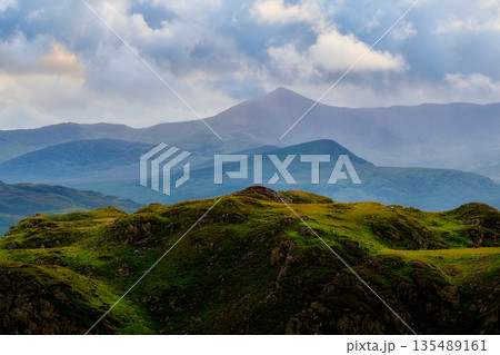 Green hills sit in the foreground, leading back to blue layered mountains. Clouds cover the sky above National Park during the daytime. Green hills sit in the foreground, leading back to blue layered mountains. Clouds cover the sky above National Park during the daytime. 135489161