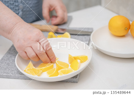 A woman's hands place a sliced lemon on a white plate A woman's hands place a sliced lemon on a white plate 135489644