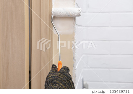 A woman wearing a glove paints a wall with white paint using a roller A woman wearing a glove paints a wall with white paint using a roller 135489731