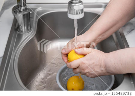 Women's hands wash a lemon in a sink under running water from a tap Women's hands wash a lemon in a sink under running water from a tap 135489738