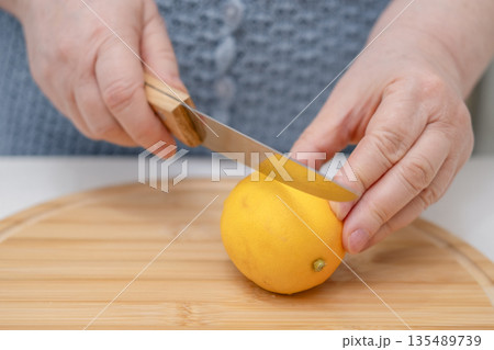 A woman's hands cut a lemon with a knife on a wooden board 135489739