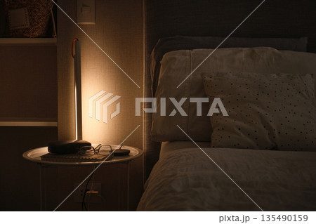 Bedroom nightstand with warm lamp light creating cozy atmosphere 135490159