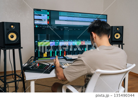 Skilled sound engineer working in home recording studio, using digital audio workstation software on large monitor and midi keyboard to compose and mix music. Skilled sound engineer working in home recording studio, using digital audio workstation software on large monitor and midi keyboard to compose and mix music. 135490344