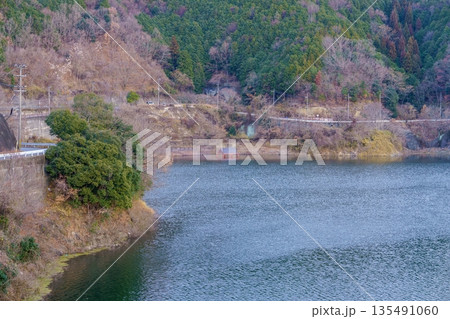 山あいのダム湖と湖面に沈む休憩所の屋根のコントラスト 135491060