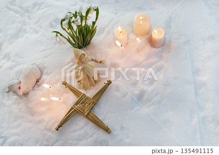 Imbolc celebration with brigid's cross, snowdrops, and candles in snow 135491115