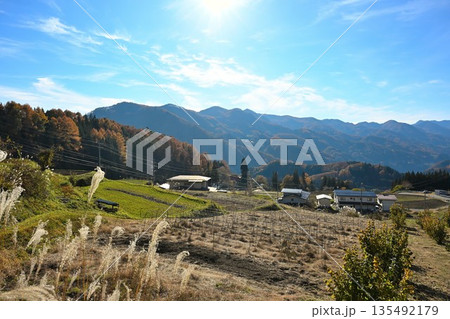 秋の山並みと草地が広がる紅葉風景（長野県長野市） 135492179
