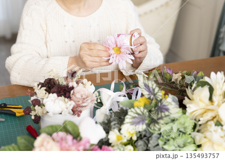 リビングで趣味のフラワーアレンジメントをするシニア女性の手元 135493757