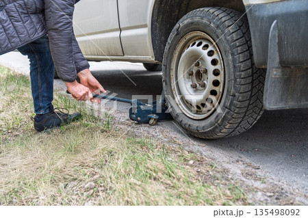 Changing a Flat Tire A Man Using a Jack to Lift the Car for Tire Replacement on Roadside 135498092