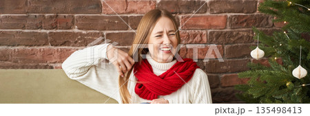 Young caucasian female enjoying christmas with warm smile by festive tree 135498413
