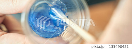 Mixing blue resin with wooden stick in clear cup for crafting or art project 135498421