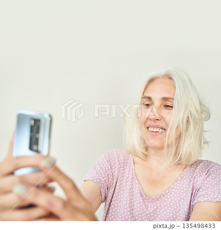 Mature caucasian female taking selfie with smartphone in casual pink polka dot Mature caucasian female taking selfie with smartphone in casual pink polka dot 135498433