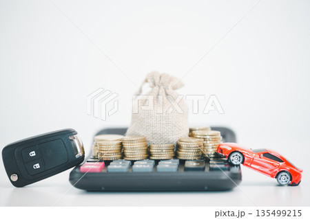 Car key fob, calculator, coin stacks and money bag with a red toy car on white background, symbolizing auto loan budgeting, down payment savings, insurance costs and purchase planning. Car key fob, calculator, coin stacks and money bag with a red toy car on white background, symbolizing auto loan budgeting, down payment savings, insurance costs and purchase planning. 135499215