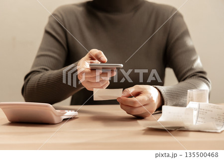 Women using smartphone calculate paper receipts on table. Calculating bills, expense tracking, personal finance Women using smartphone calculate paper receipts on table. Calculating bills, expense tracking, personal finance 135500468