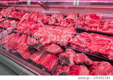 Chilled fresh meat on display with red lighting. Fresh cuts of beef and pork are organized in a meat display case at a local shop. The vibrant red meat is visible under bright lights. High quality 135501193