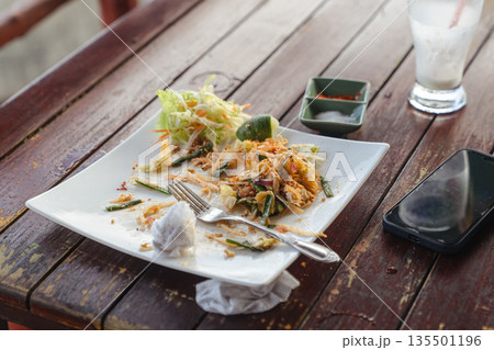 Lunch leftovers - Pad Thai noodles in a white square plate on a wooden table in an outdoor restaurant on the street. Delicious Thai street food. High quality photo Lunch leftovers - Pad Thai noodles in a white square plate on a wooden table in an outdoor restaurant on the street. Delicious Thai street food. High quality photo 135501196