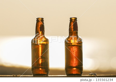 Two bottles of beer at sunset on a table on the beach in close-up. The concept of a party and a vacation on a trip. High quality photo 135501234
