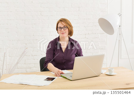 Successful middle-aged businesswoman in the office. Woman using laptop computer and smartphone. 135501464