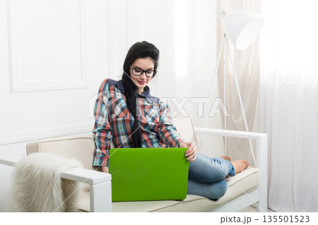 Freelancer woman works at home. Home office, freelance. Brunette girl with laptop in modern interior at white couch. High key. 135501523