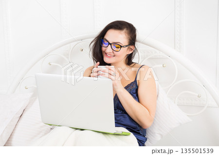 Sunday morning in bed. Middle aged woman surfing internet at her laptop computer. High key. Sunday morning in bed. Middle aged woman surfing internet at her laptop computer. High key. 135501539