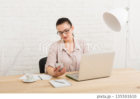 Middle-aged business woman in office with smartphone. Female using mobile phone at workplace, copy space. Communication concept 135501610