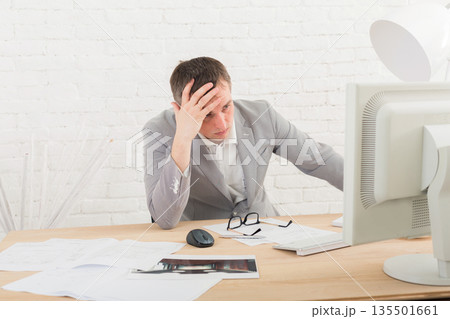 Working problems, issues of business. Young businessman in white modern office interior, thoughtful, sitting at computer table. 135501661