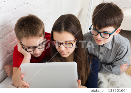 Group of kids in eye glasses look into tablet. Children computer games, social networks and media addiction concept. Girl and boys with tablet. Communication technologies. Group of kids in eye glasses look into tablet. Children computer games, social networks and media addiction concept. Girl and boys with tablet. Communication technologies. 135501664
