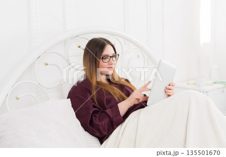 Sunday morning in bed. Young woman in surfing internet at her tablet pc, copy space Sunday morning in bed. Young woman in surfing internet at her tablet pc, copy space 135501670