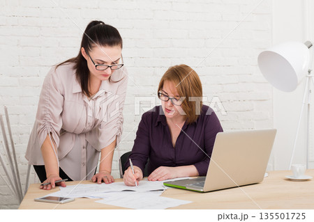 Middle-aged women in office. Teamwork, business communication. Two architects designers in team work discuss project. Start up discussion. Female coworkers. Middle-aged women in office. Teamwork, business communication. Two architects designers in team work discuss project. Start up discussion. Female coworkers. 135501725