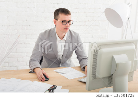 Young businessman working with laptop in modern white office interior. Handsome man, successful employee at work with computer. Lifestyle portrait 135501728