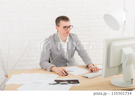 Young businessman working with laptop in modern white office interior. Handsome man in suit, successful employee at work with computer. Lifestyle portrait 135501734