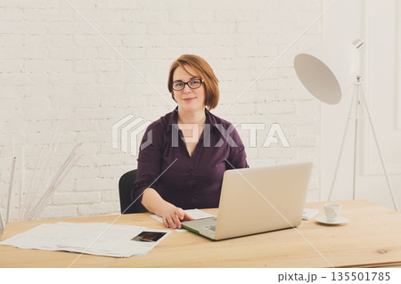 Middle-aged Woman in the office. Female architect using laptop computer and smartphone. Office worker. Redhead caucasian woman in protective glasses with computer. High-key, soft tone. 135501785