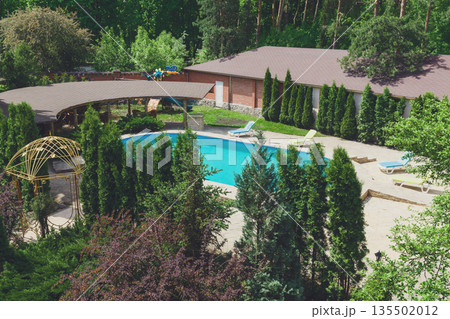 Luxury swimming pool beside the modern hotel and spa resort. Landscape design of territory. Beautiful trees and bushes, park and garden. Luxury swimming pool beside the modern hotel and spa resort. Landscape design of territory. Beautiful trees and bushes, park and garden. 135502012