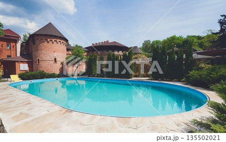 Luxury swimming pool beside the hotel in medieval british castle style. Landscape design of resort territory. Blue water in summer park. 135502021