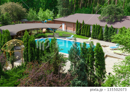 Luxury swimming pool beside the modern hotel and spa resort. Landscape design of resort territory. Beautiful trees and bushes. Luxury swimming pool beside the modern hotel and spa resort. Landscape design of resort territory. Beautiful trees and bushes. 135502073