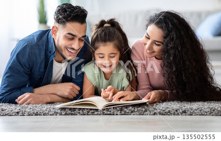 Portraif Of Happy Arabic Family Of Three Reading Book Together At Home, Relaxing On Floor In Living Room, Middle Eastern Mom And Dad Spending Time With Their Kid, Enjoying Domestic Leisure, Closeup Portraif Of Happy Arabic Family Of Three Reading Book Together At Home, Relaxing On Floor In Living Room, Middle Eastern Mom And Dad Spending Time With Their Kid, Enjoying Domestic Leisure, Closeup 135502555