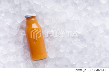 Orange detox juice in glass bottle on ice cubes background, panorama 135502617