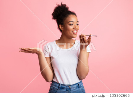 Happy young black lady using voice assistant on smartphone, gesturing isolated over pastel pink studio wall, copyspace Happy young black lady using voice assistant on smartphone, gesturing isolated over pastel pink studio wall, copyspace 135502666