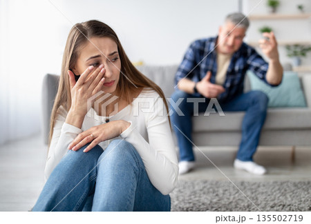 Emotional or psychological domestic violence concept. Mature man abusing his depressed wife, shouting, humiliating and threatening her, middle aged woman crying on floor at home Emotional or psychological domestic violence concept. Mature man abusing his depressed wife, shouting, humiliating and threatening her, middle aged woman crying on floor at home 135502719