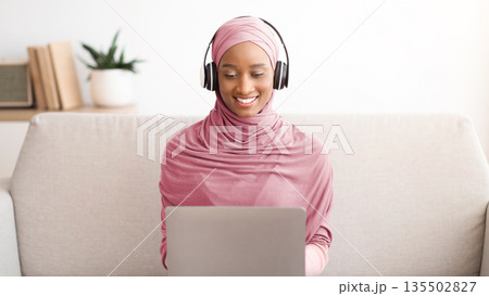 Smiling Muslim businesswoman in hijab and headset having video call on laptop at home office, talking with coworkers on web. Young Arab freelancer taking part in online meeting Smiling Muslim businesswoman in hijab and headset having video call on laptop at home office, talking with coworkers on web. Young Arab freelancer taking part in online meeting 135502827