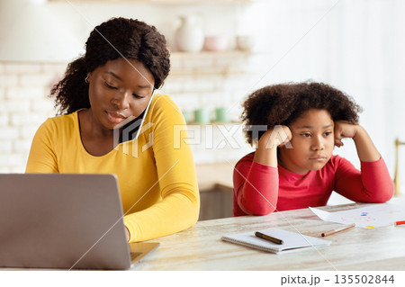 Lack Of Attention. Bored Little Black Girl Sitting Next To Her Busy Mom Working With Laptop And Cellphone In Kitchen, Upset African American Child Feeling Lonely And Depressed, Free Space Lack Of Attention. Bored Little Black Girl Sitting Next To Her Busy Mom Working With Laptop And Cellphone In Kitchen, Upset African American Child Feeling Lonely And Depressed, Free Space 135502844