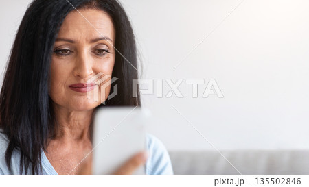 Technology Concept. Closeup portrait of smiling woman holding smartphone, making video call sitting at home. Distant Communication. Happy woman surfing internet, watching funny video, selective focus Technology Concept. Closeup portrait of smiling woman holding smartphone, making video call sitting at home. Distant Communication. Happy woman surfing internet, watching funny video, selective focus 135502846