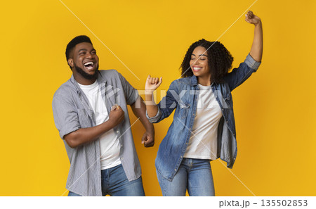 Dance Fun. Cheerful African American Couple Fooling Together, Dancing And Laughing, Posing Over Yellow Background With Empty Space Dance Fun. Cheerful African American Couple Fooling Together, Dancing And Laughing, Posing Over Yellow Background With Empty Space 135502853